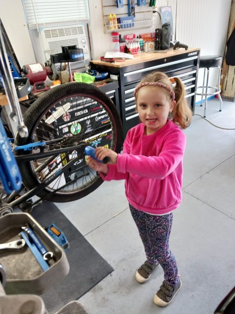 John’s granddaughter holding a bicycle wheel in the repair shop